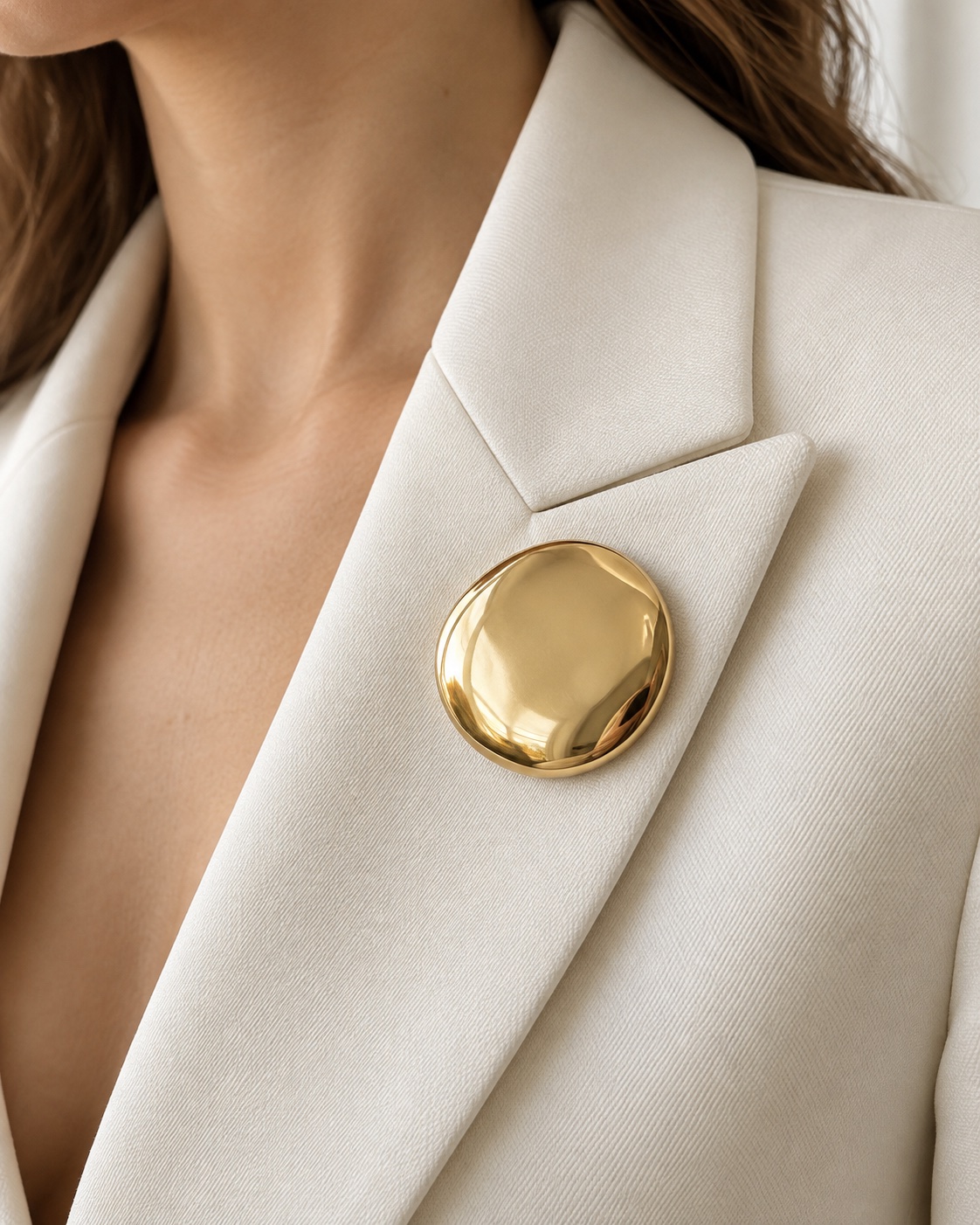 Polished gold-tone round disc brooch on an ivory blazer lapel