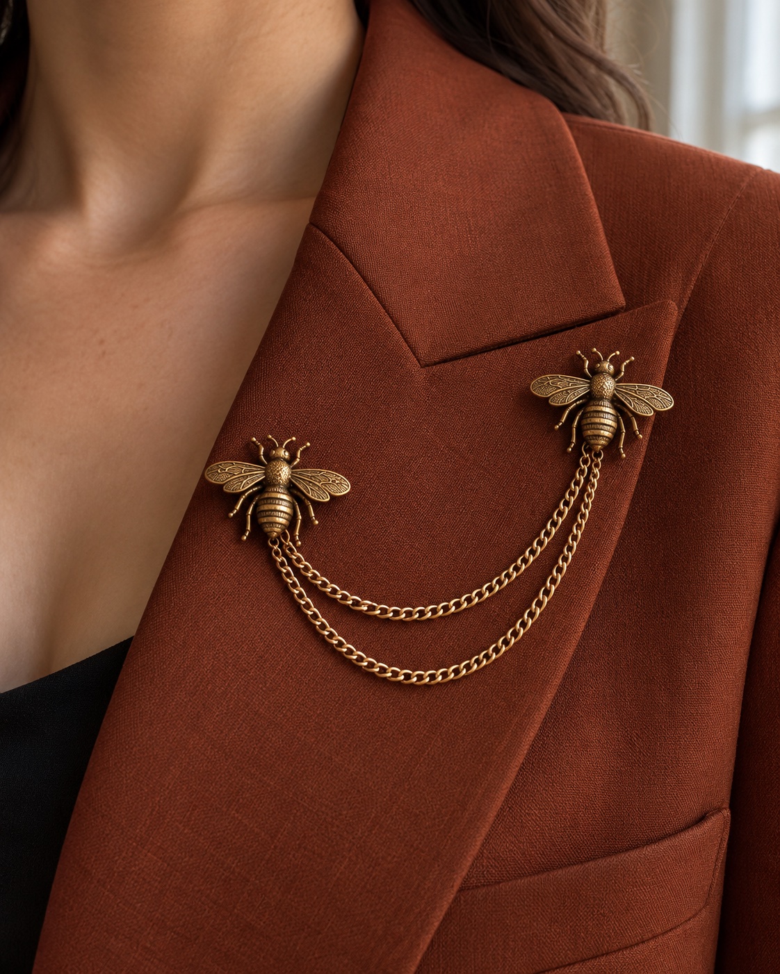 Two antique-gold bee pins joined by two draped chains on rust tailoring